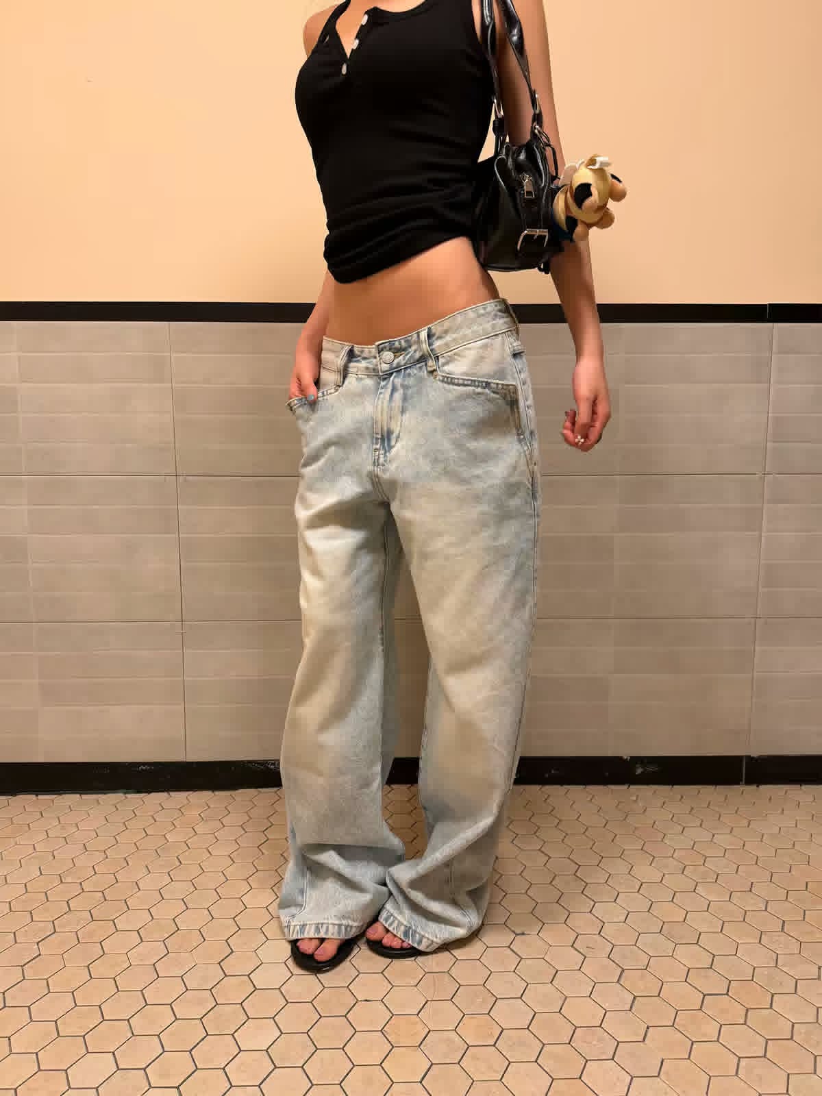 Model wearing a black sleeveless top with relaxed light-wash jeans and carrying a black handbag.