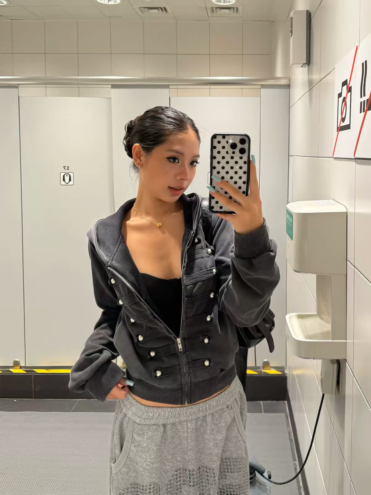 Model wearing a black cropped embellished jacket with gray sweatpants in a mirror selfie.