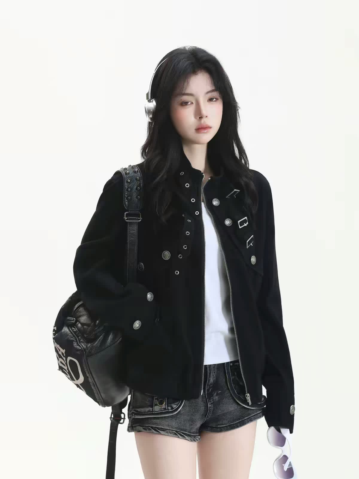 Model wearing a black embellished jacket with denim shorts and carrying a black shoulder bag