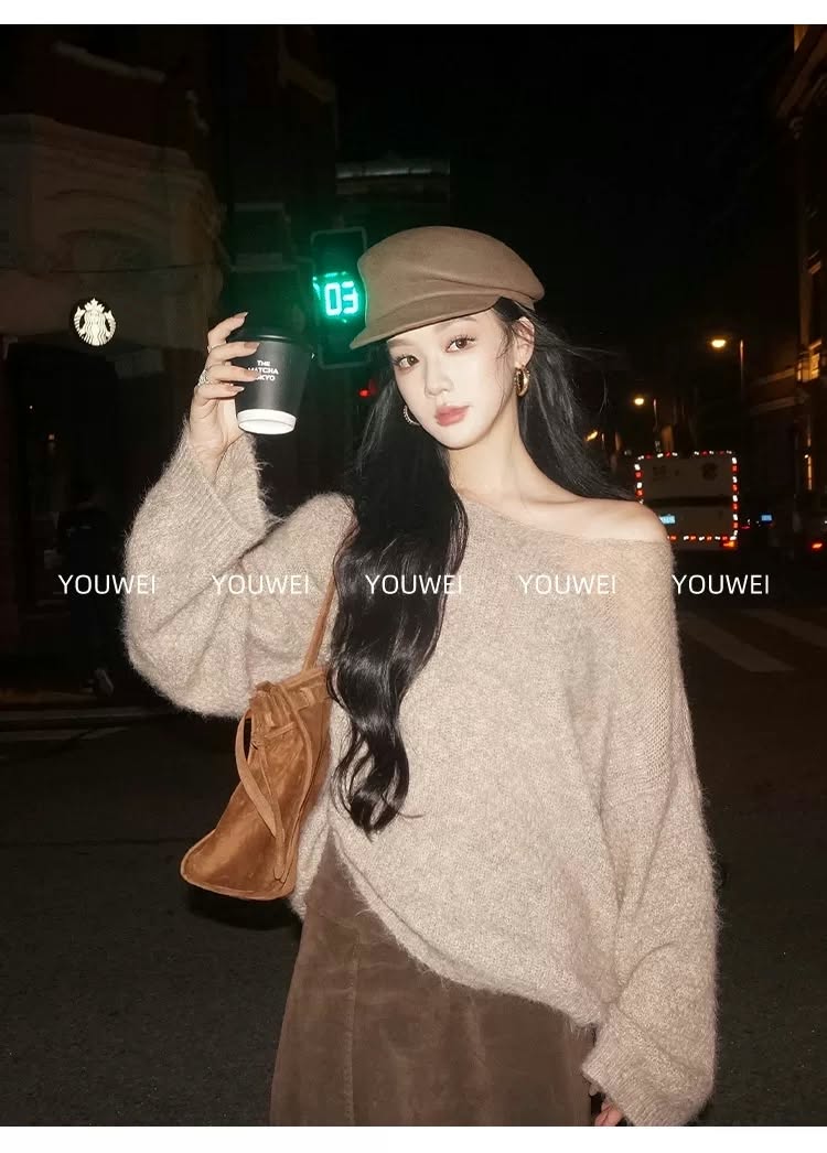 Woman modeling a cozy off-shoulder knit sweater with a brown cap and shoulder bag at night