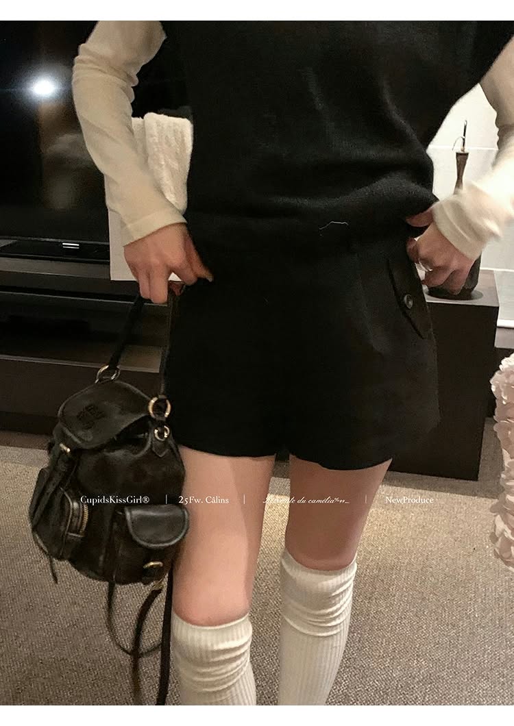 Model wearing a black layered outfit with a white blouse, black bottoms, knee-high leg warmers, and a black handbag.